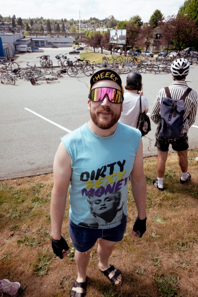 A cyclist with sunglasses looks at the camera wearing a shirt that says "Dirty Sexy Money."