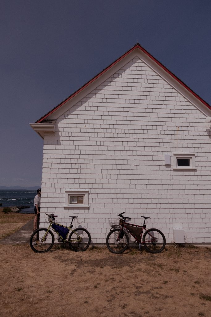 Two bike-camping bikes sit against the outer wall of a small white house.