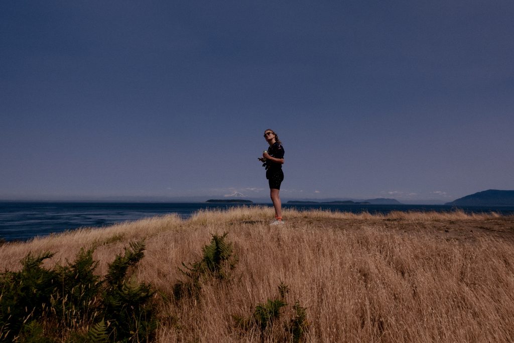 A camper smiles and looks at the camera in front of the ocean.