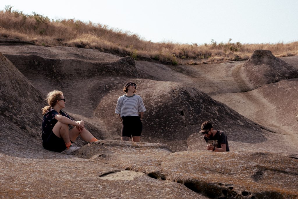 Three campers sit by the ocean and look out towards it.