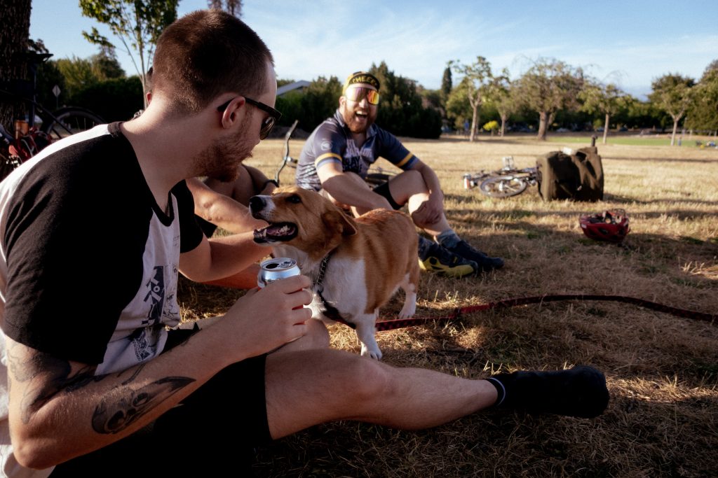 A corgi greets a cyclist drinking a beer.