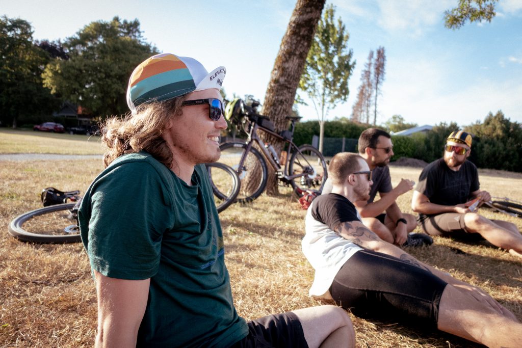 Four cyclists hang out in a park with bikes behind them.