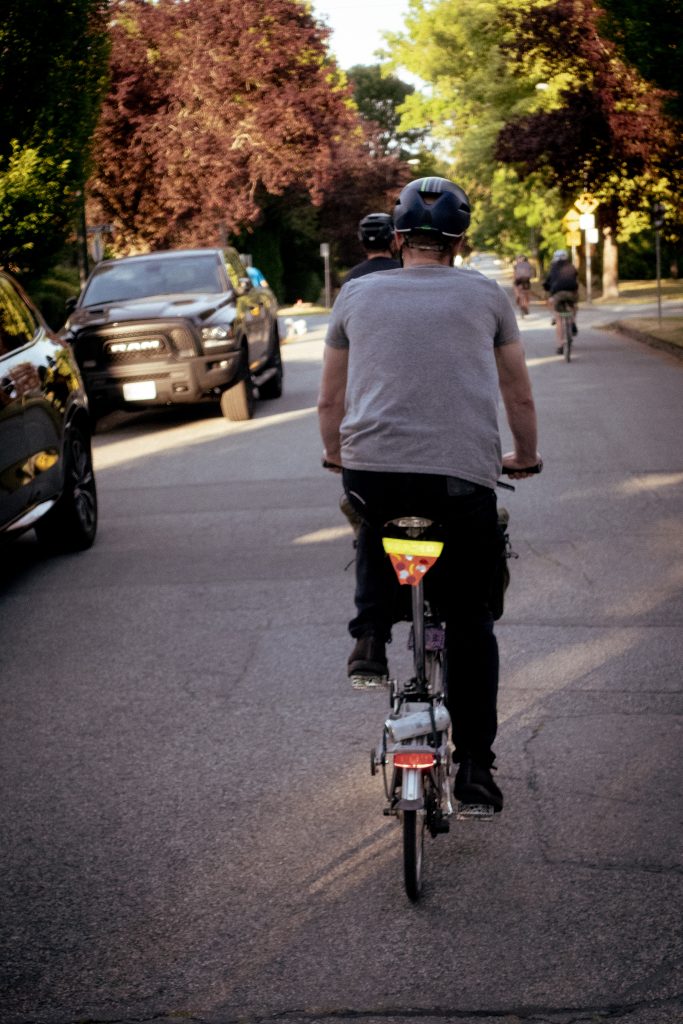 A cyclist rides a bike down a street in a group. Their bike is small and has a pizza-shaped reflector.