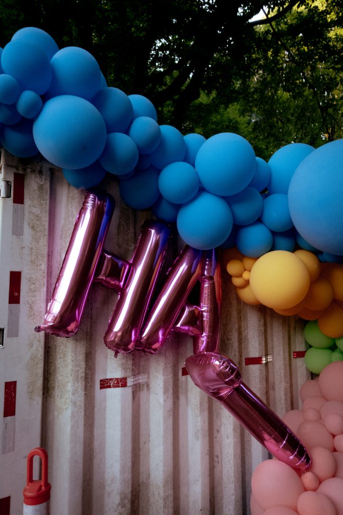 A random balloon display with multiple colours hangs off a shipping container. A second set of balloons spell out the word hat.