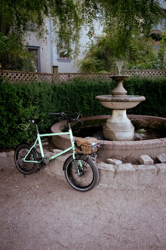 A small bicycle rests against a small water fountain.