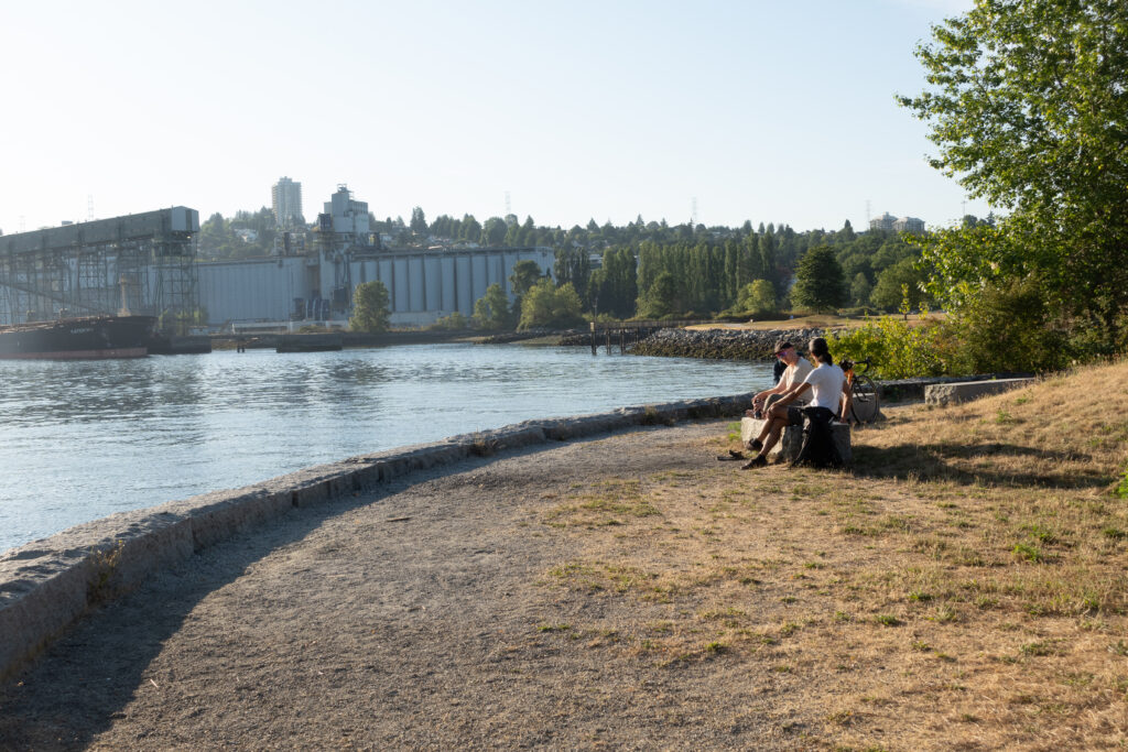 A group of cyclists sit by the ocean in Vancouver, sipping coffee together.