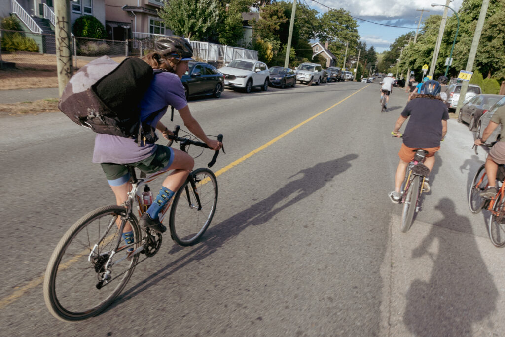 A group of 4 cyclists are riding down the road in Vancouver, the one closet to the camera have a large pack of recycling as a back pakc.