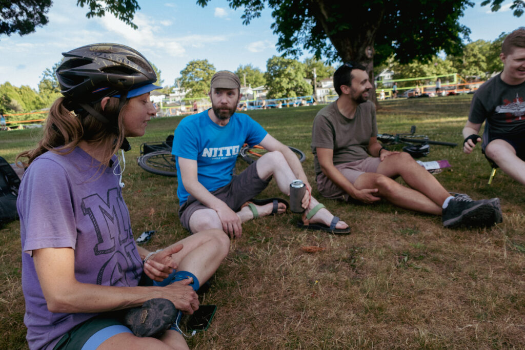 A group of cyclists sit chatting and laughing at a park.