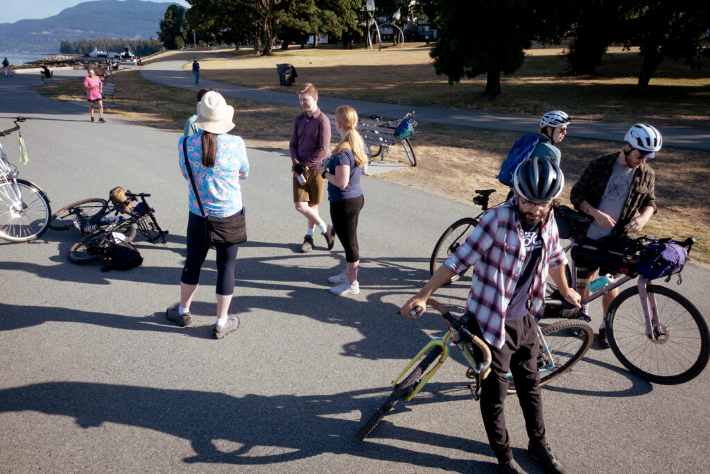 A group of cyclists stand by the seawall in Vancouver leaning against their bikes and talking