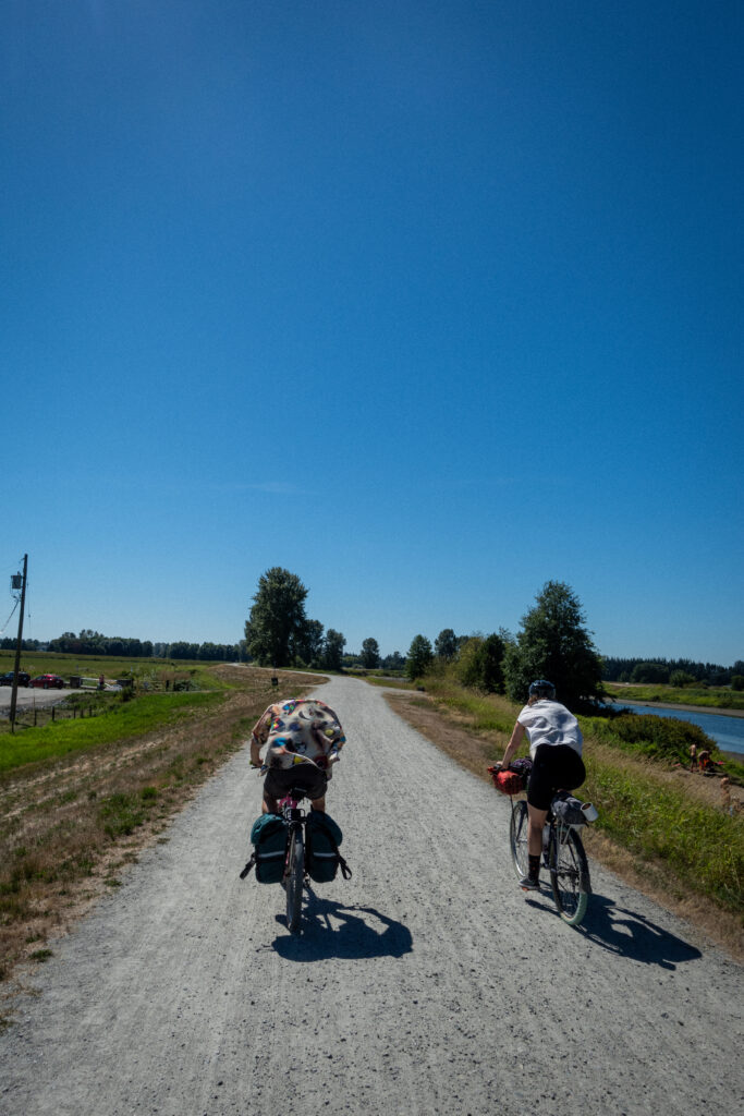 Two cyclists bike on a dirt road in the heat.