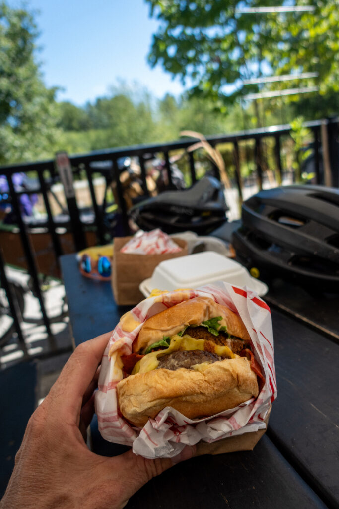 A veggie burger with two patties is in the hand of a cyclist.