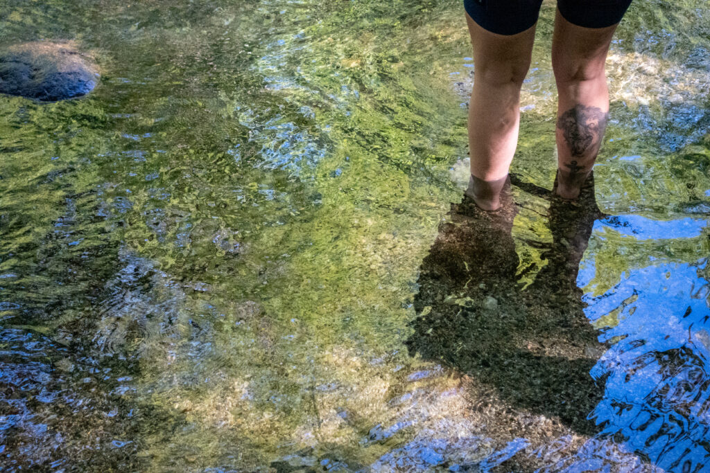 A cyclist stands in a river. Only their legs are shown.