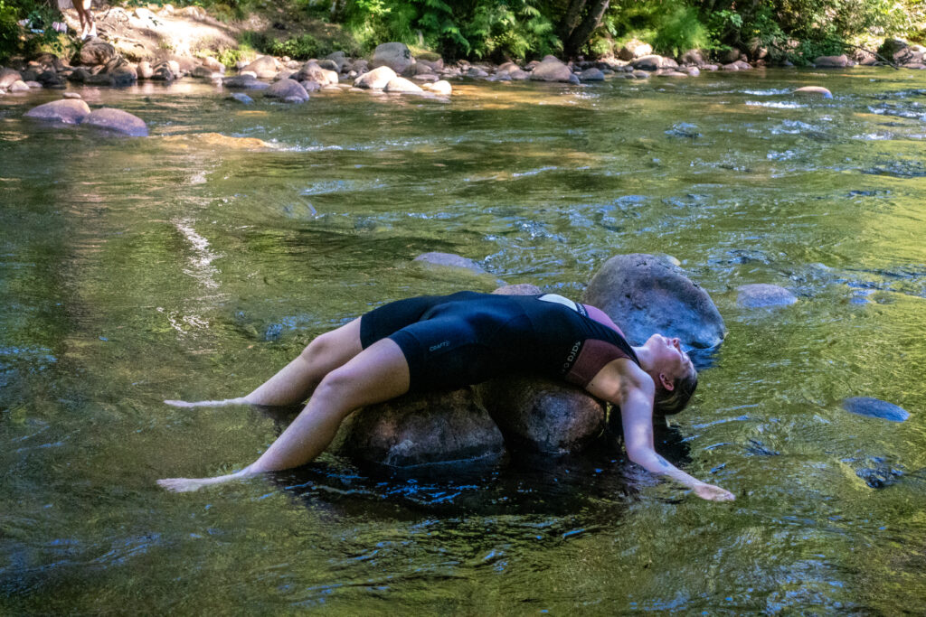 A cyclist lays on some rocks in a river as they cool themselves off during a hot day